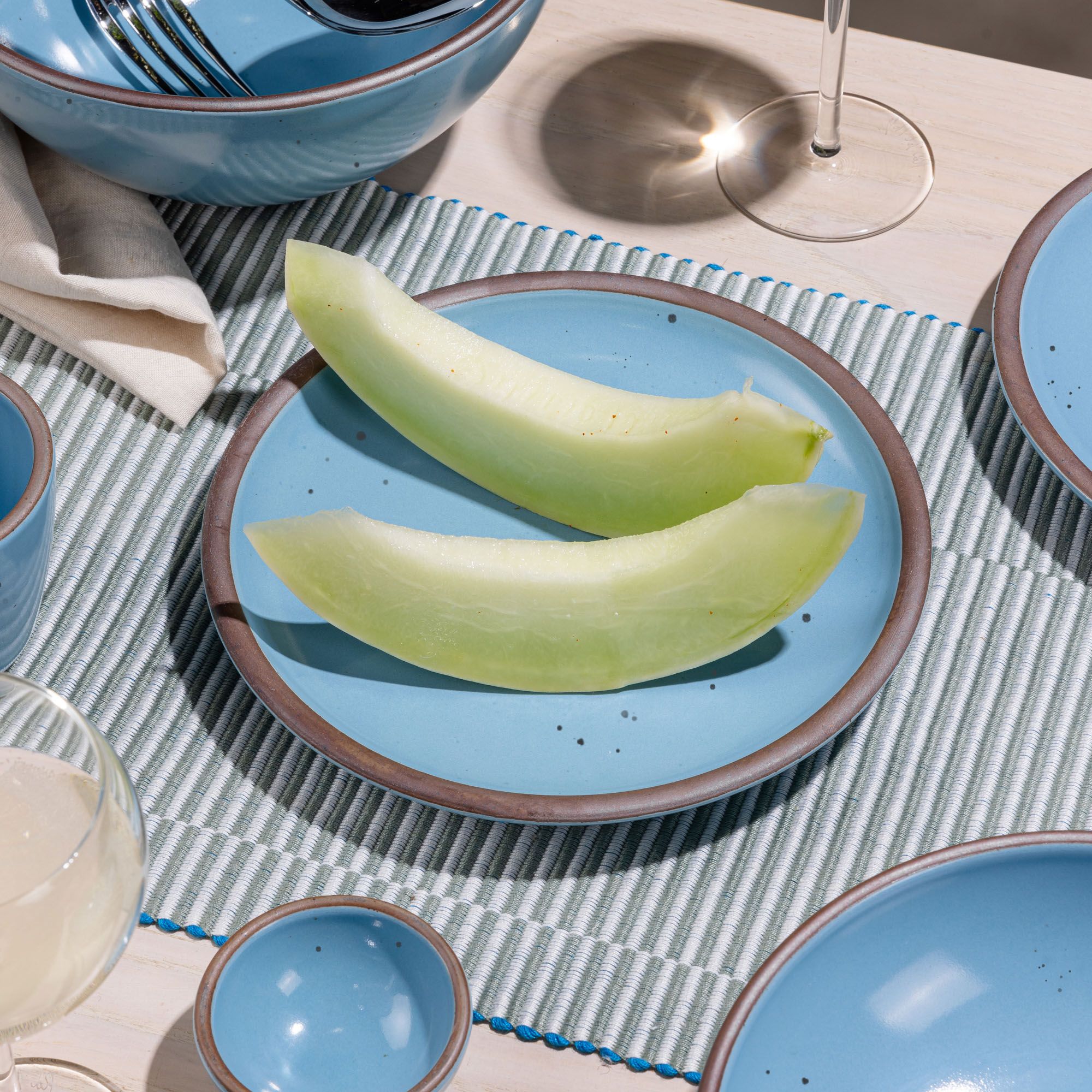 Melon slices are sitting on a ceramic robin's egg blue color on a striped placemat.