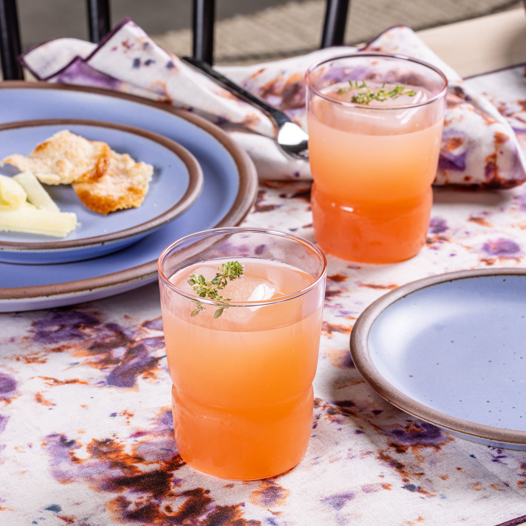 2 tumbler glasses that widen at the top in a pink colors on a table with periwinkle ceramic plates.