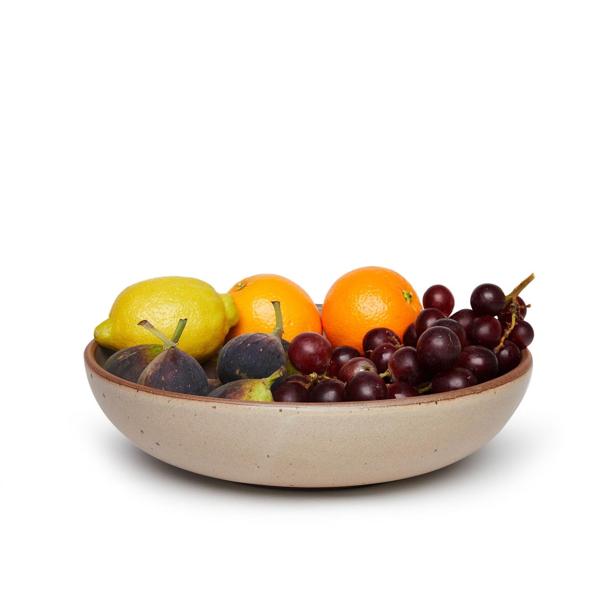 A large shallow serving ceramic bowl in a warm pale brown color featuring iron speckles and an unglazed rim, with a fruit medley