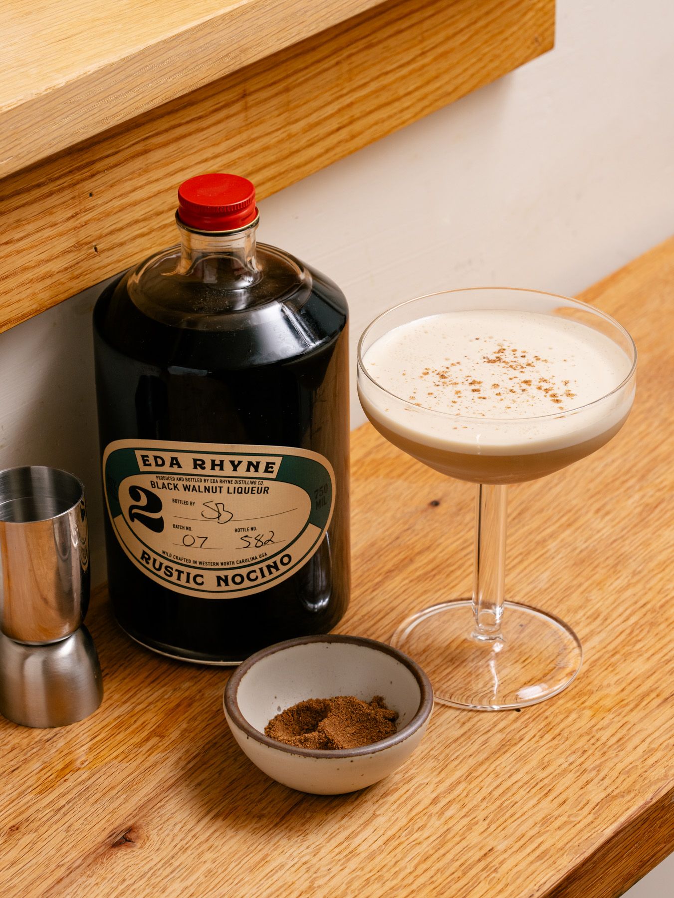 A bottle of liquor sits next to a martini glass filled with a cocktail, and a bitty bowl in the front.