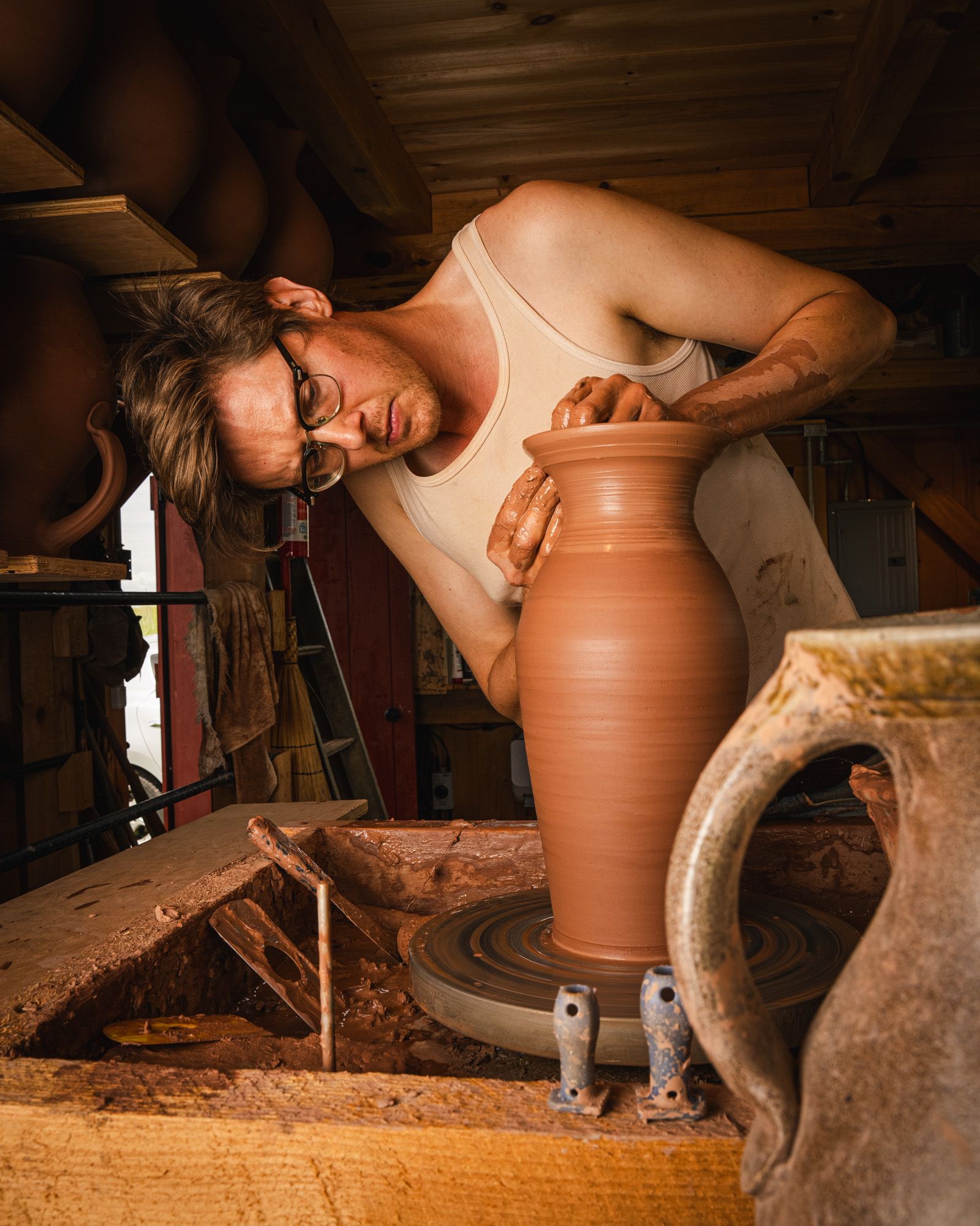 John forming a large pitcher vase on a potter's wheel in his studio.
