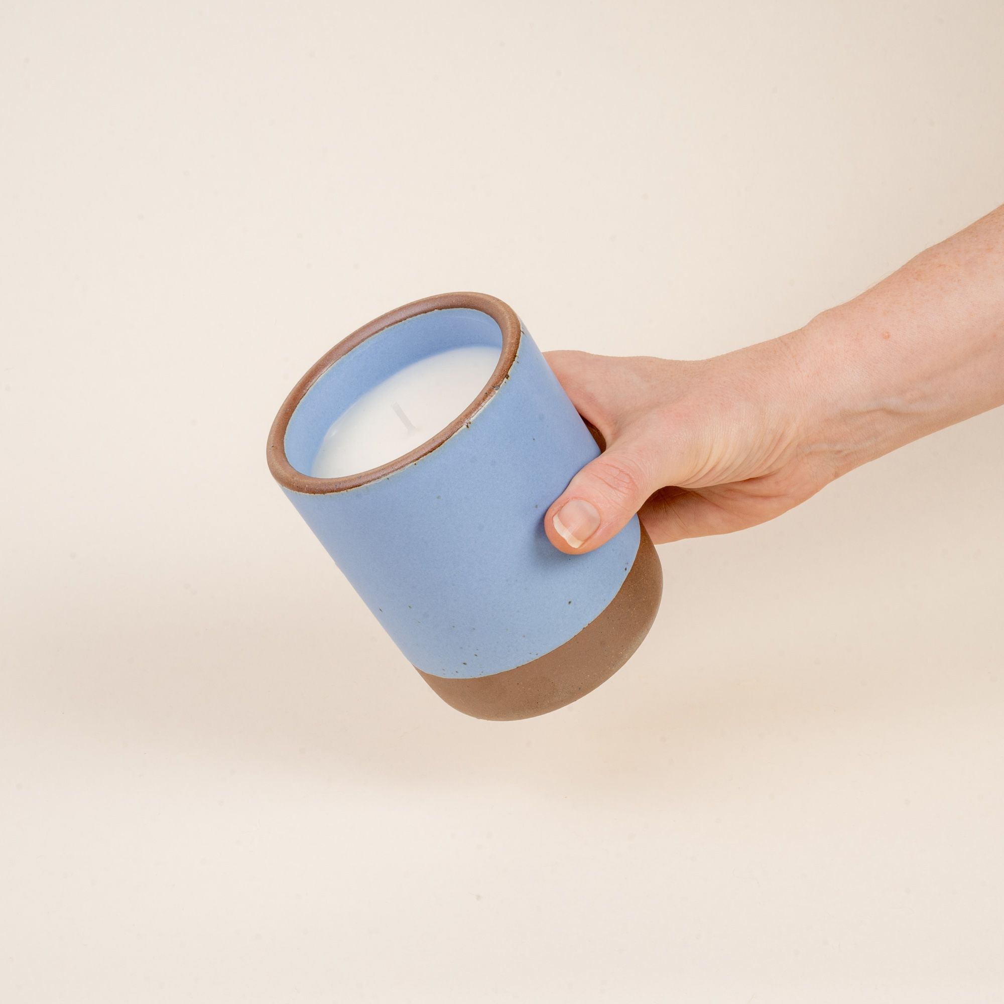 A hand holds out a large ceramic vessel in a periwinkle color with candle inside.