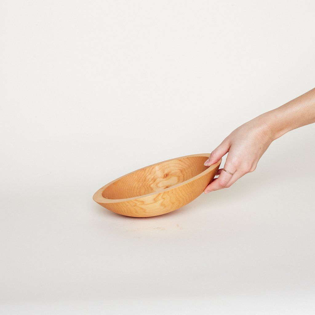 A hand touches the edge and side of a small light-colored wooden bowl