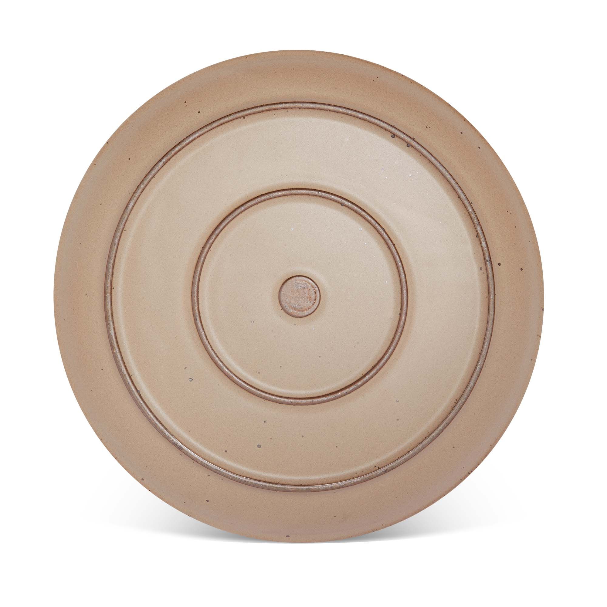 Bottom of a large ceramic platter in a warm pale brown color featuring iron speckles and an unglazed rim