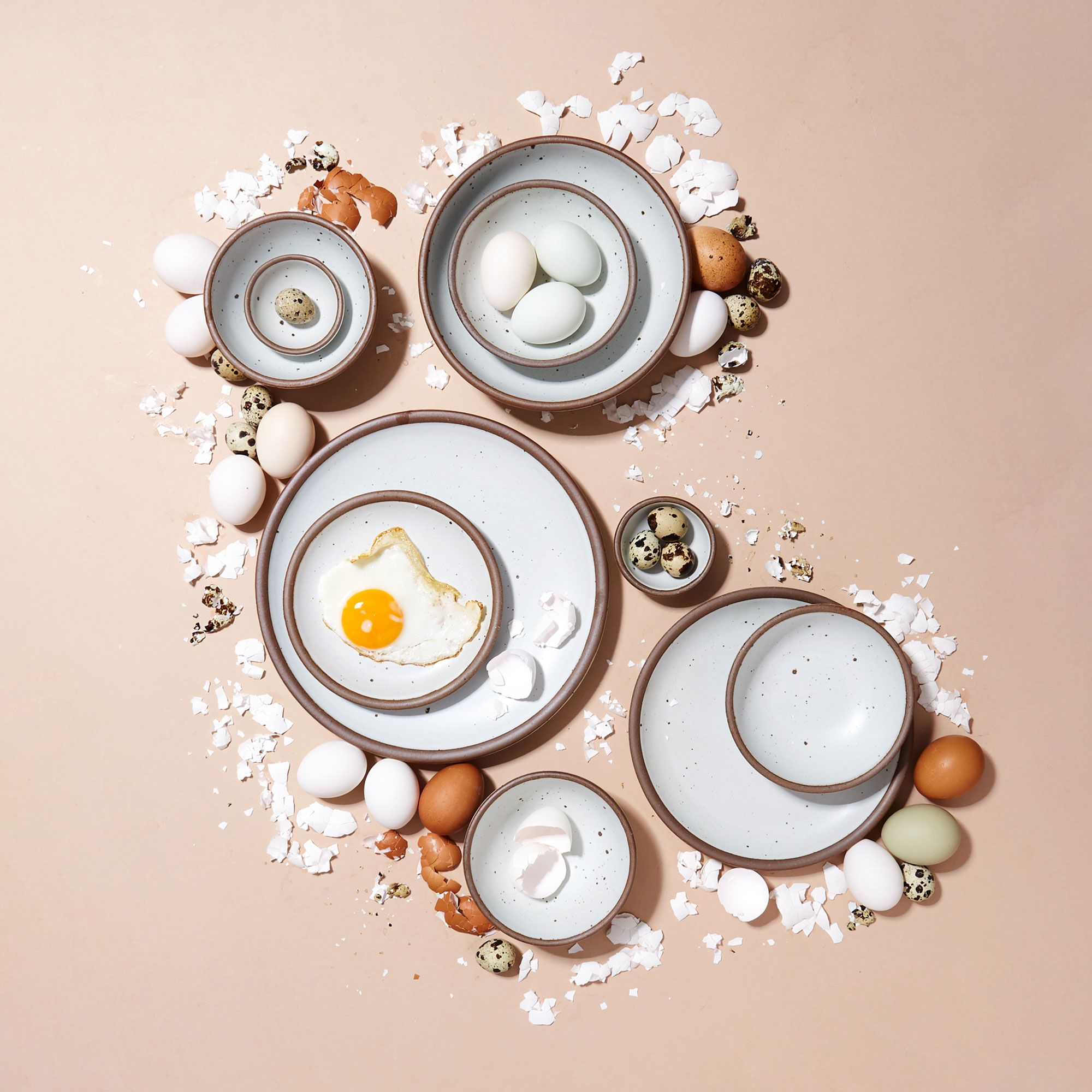Eggshell plates and bowls with cooked and broken eggs against a warm light brown background