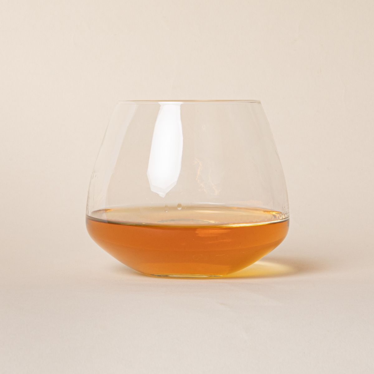 Clear glass whiskey snifter with a rounded base, filled halfway with a drink