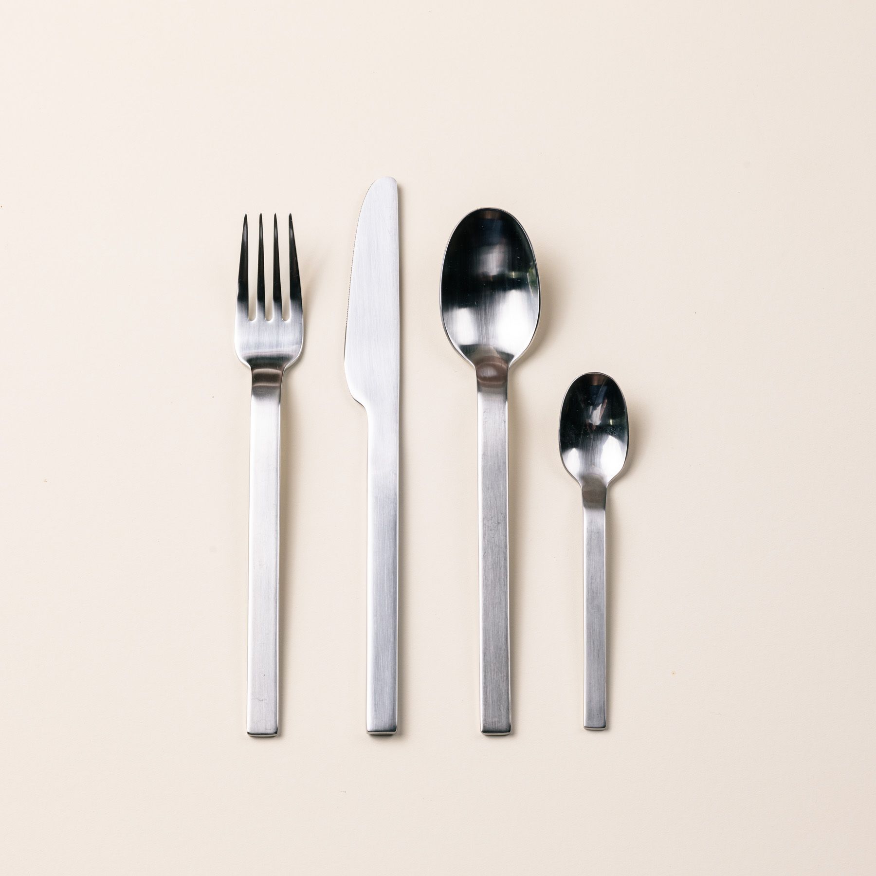 A lineup of a steel fork, knife, spoon, and teaspoon