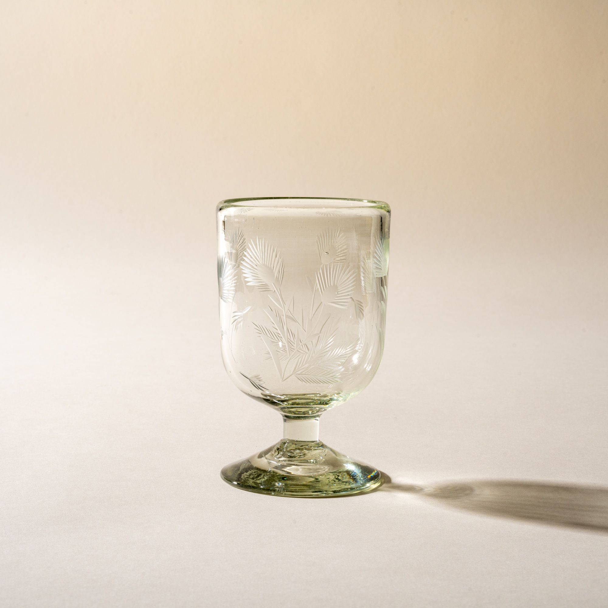 A clear short wine glass made of recycled glass with etched thistle designs on it