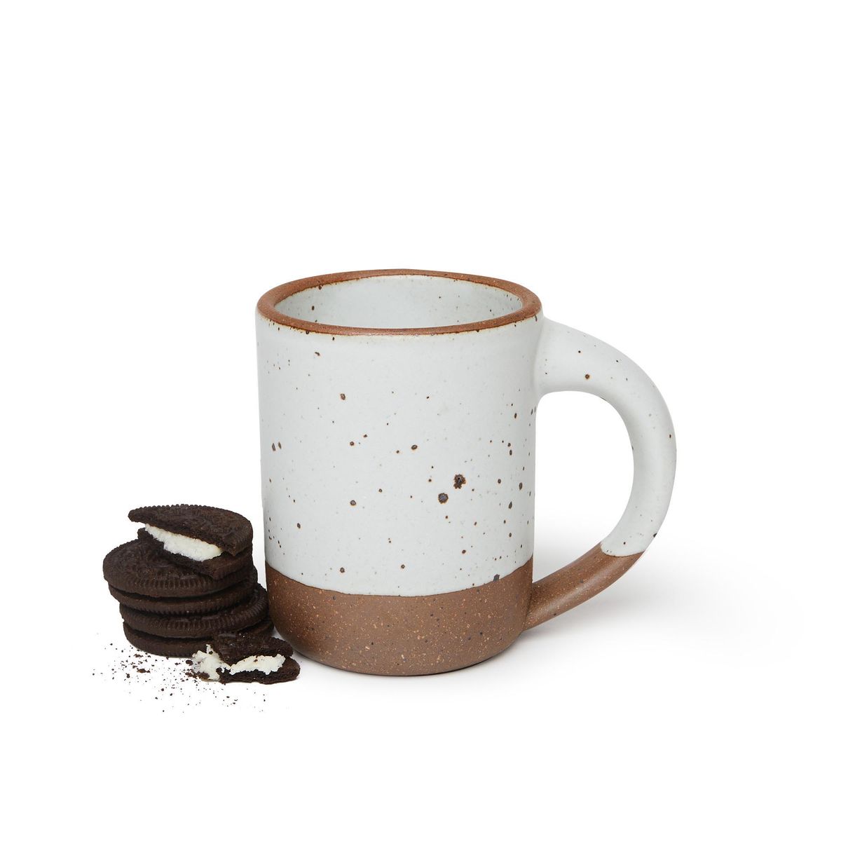A stack of cookies next to a medium sized ceramic mug with handle in a cool white color featuring iron speckles and unglazed rim and bottom base.