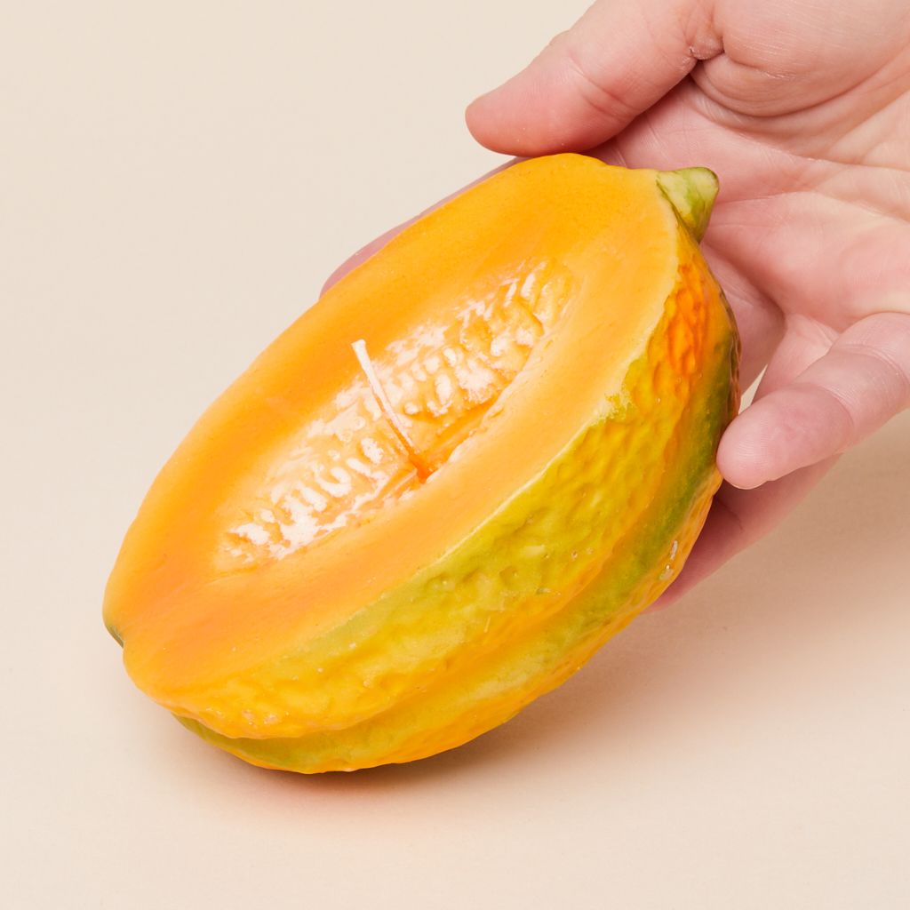 A candle that looks like a cut cantaloupe, held in a hand