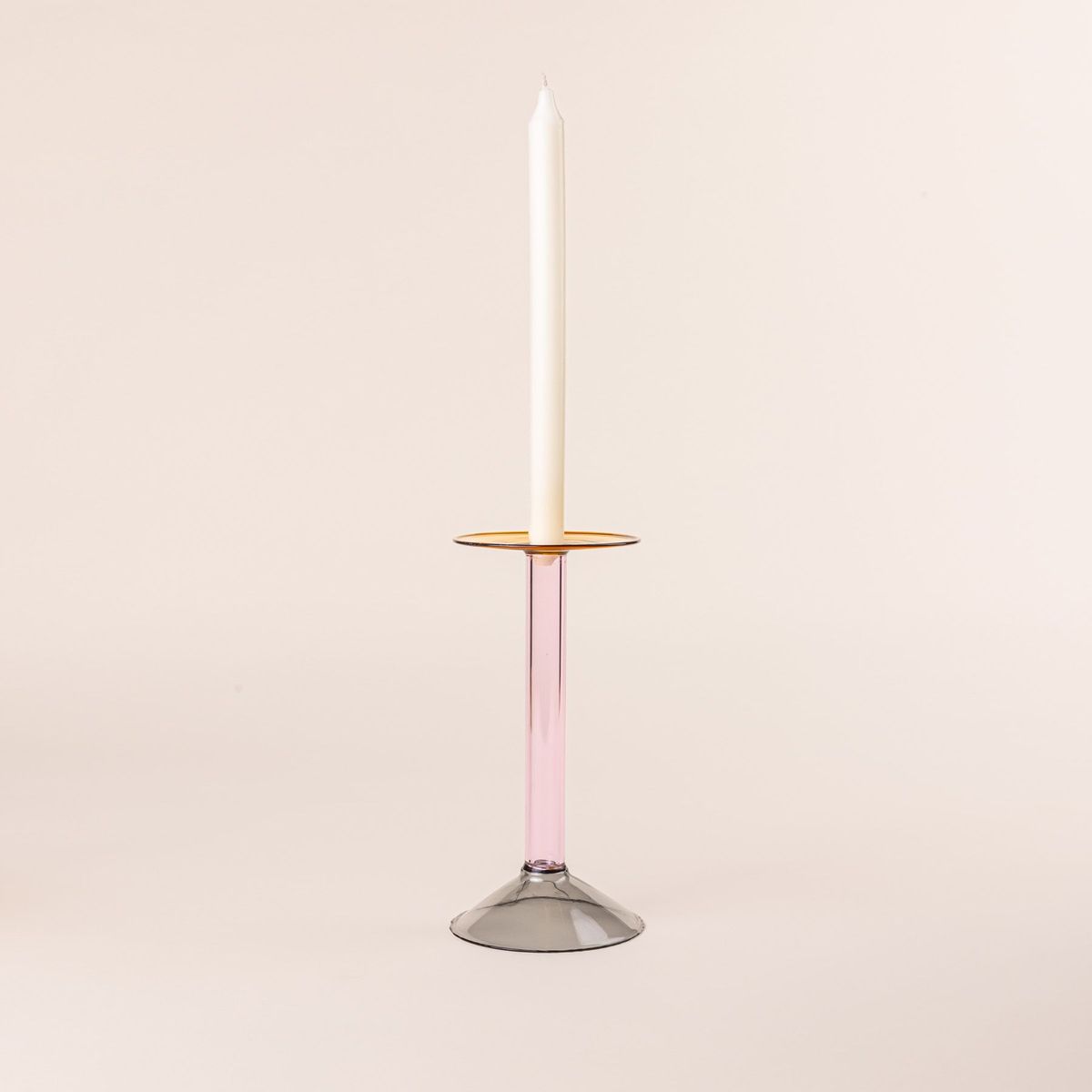 A tall modern angular glass candle holder in yellow, pink, and grey colorblocks with a cream taper candle