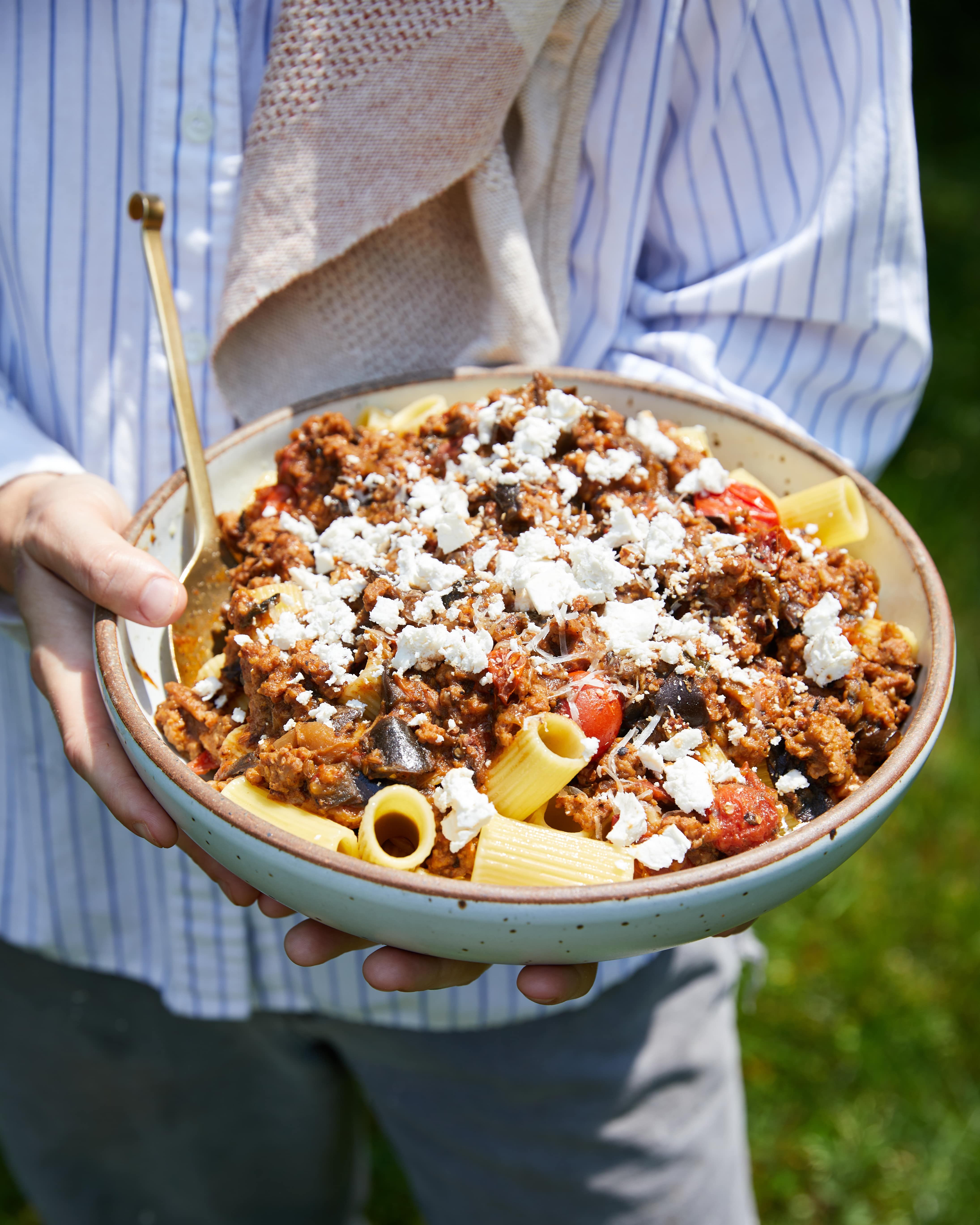 A person holds a large serving bowl of rigatoni and eggplant alla norma