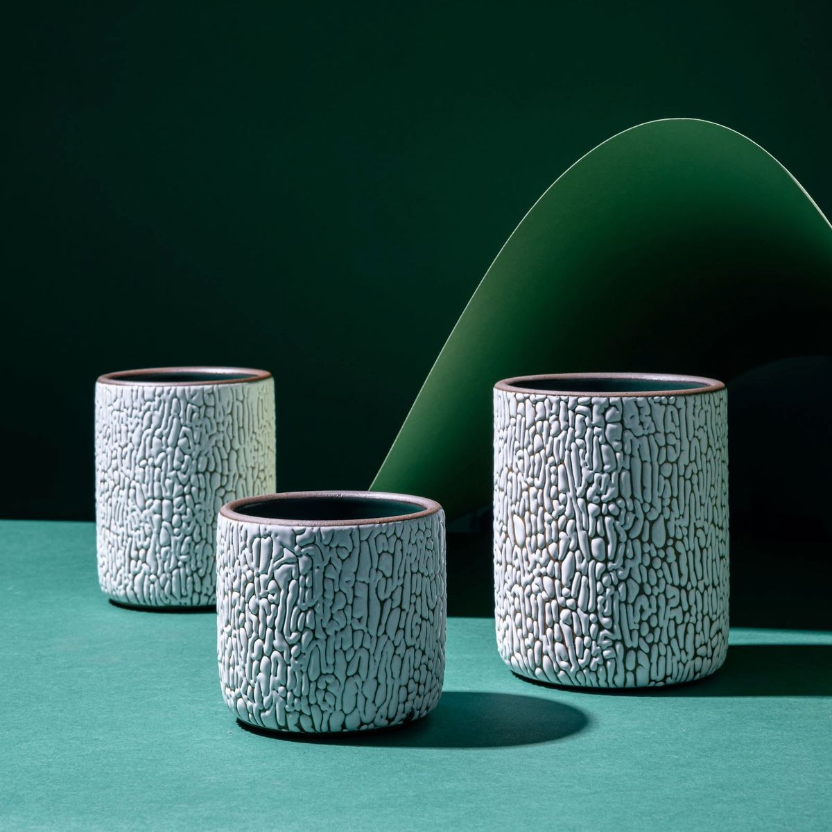 Three white ceramic vessels in Small, Medium, and Big with cracked texture and the interior being dark teal. Artfully arranged in a moody studio setting.