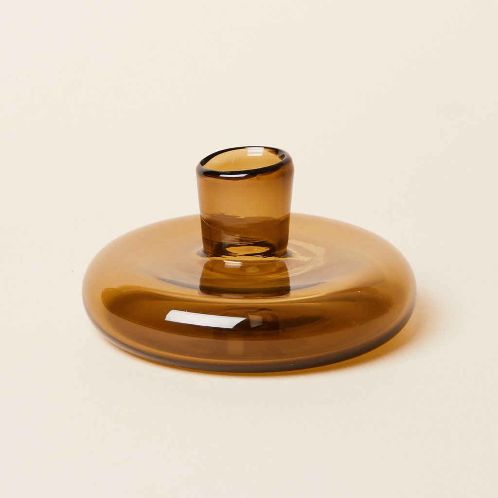 A clear brown candle holder made of a disc-like base with a small cup for the candle at center