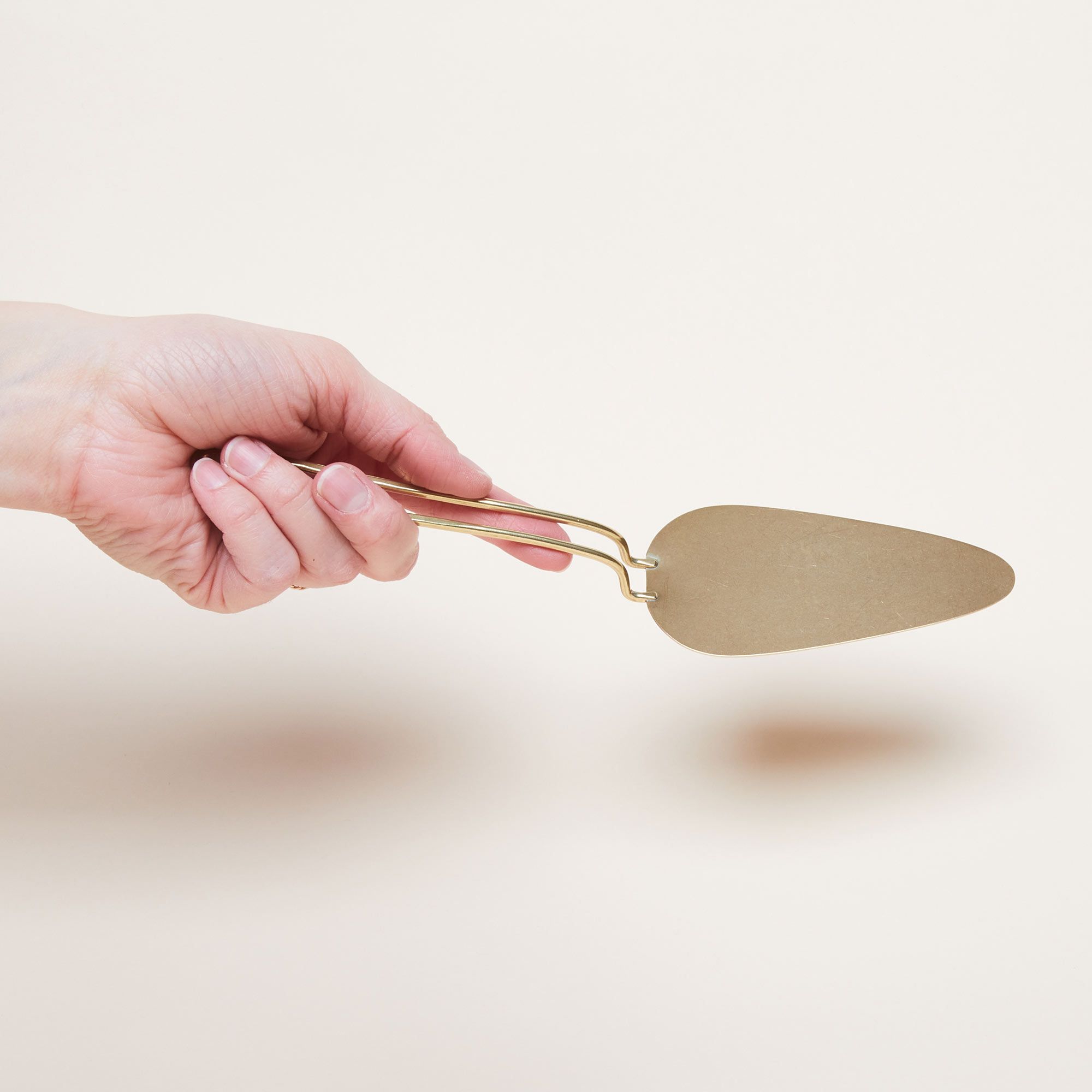 A hand holds a brass pie server that has a triangular part for lifting