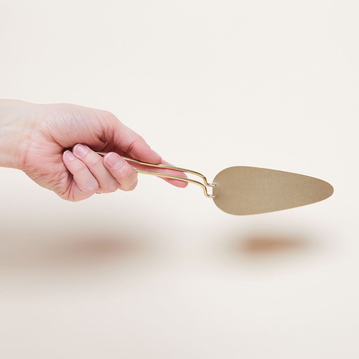 A hand hold the handle of a brass pie server