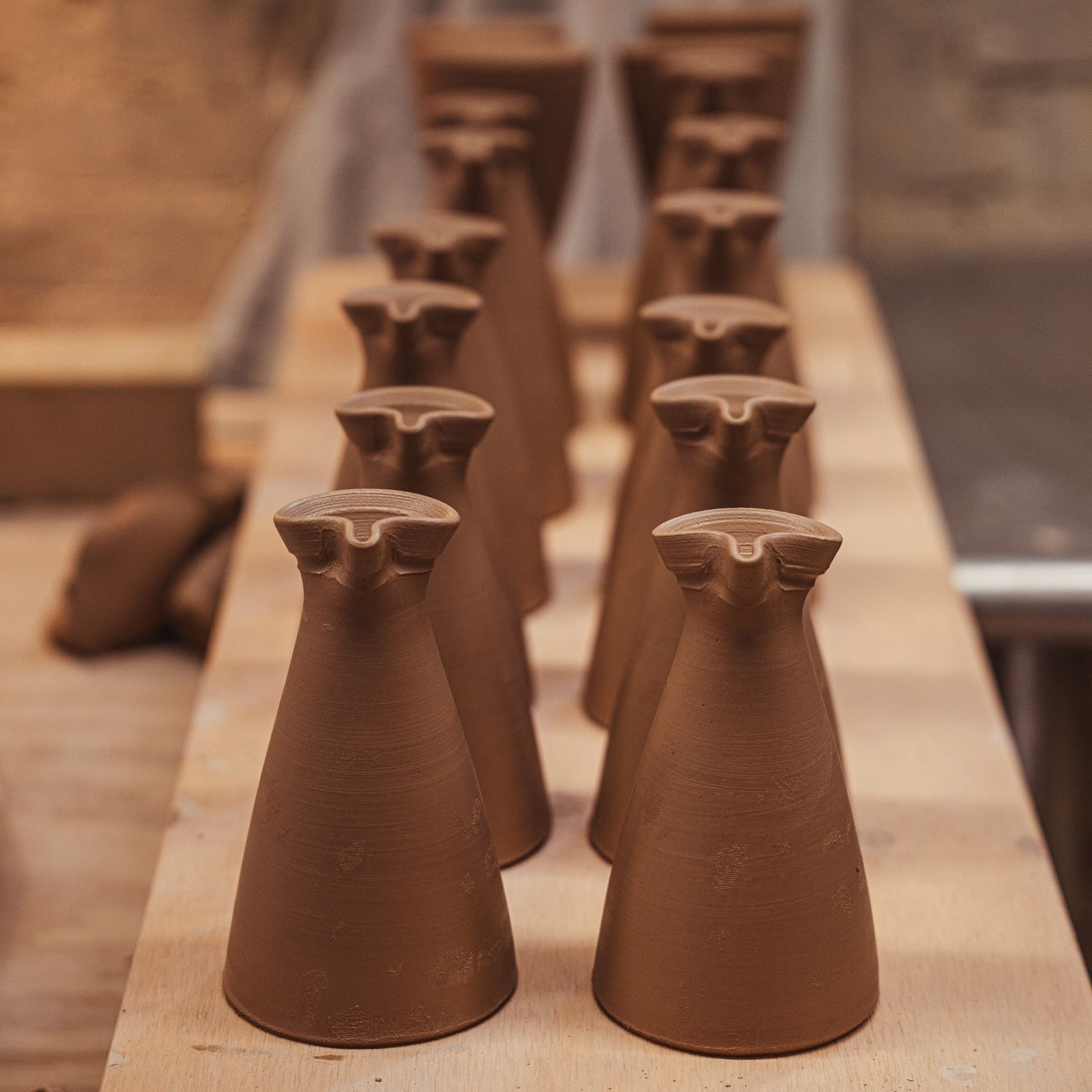 Recently handthrown workshop creamers lined in a row and sitting on a wood board to dry.