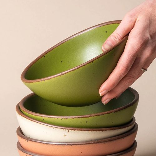 A hand picks up a Soup Bowl in Fiddlehead from a stack of other East Fork bowls