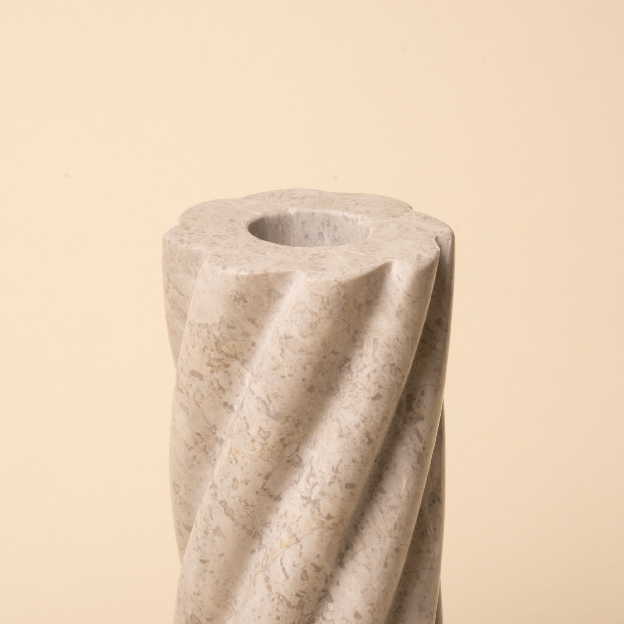 Close-up of a light gray stone candle holder with spiral grooves and a round opening for a taper candle.