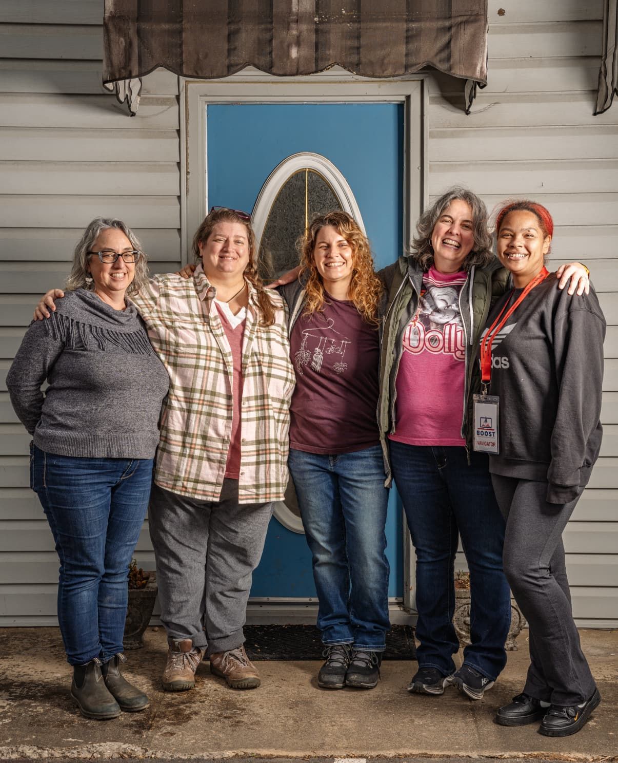 Five people gather together smiling in front of a building with a blue door.