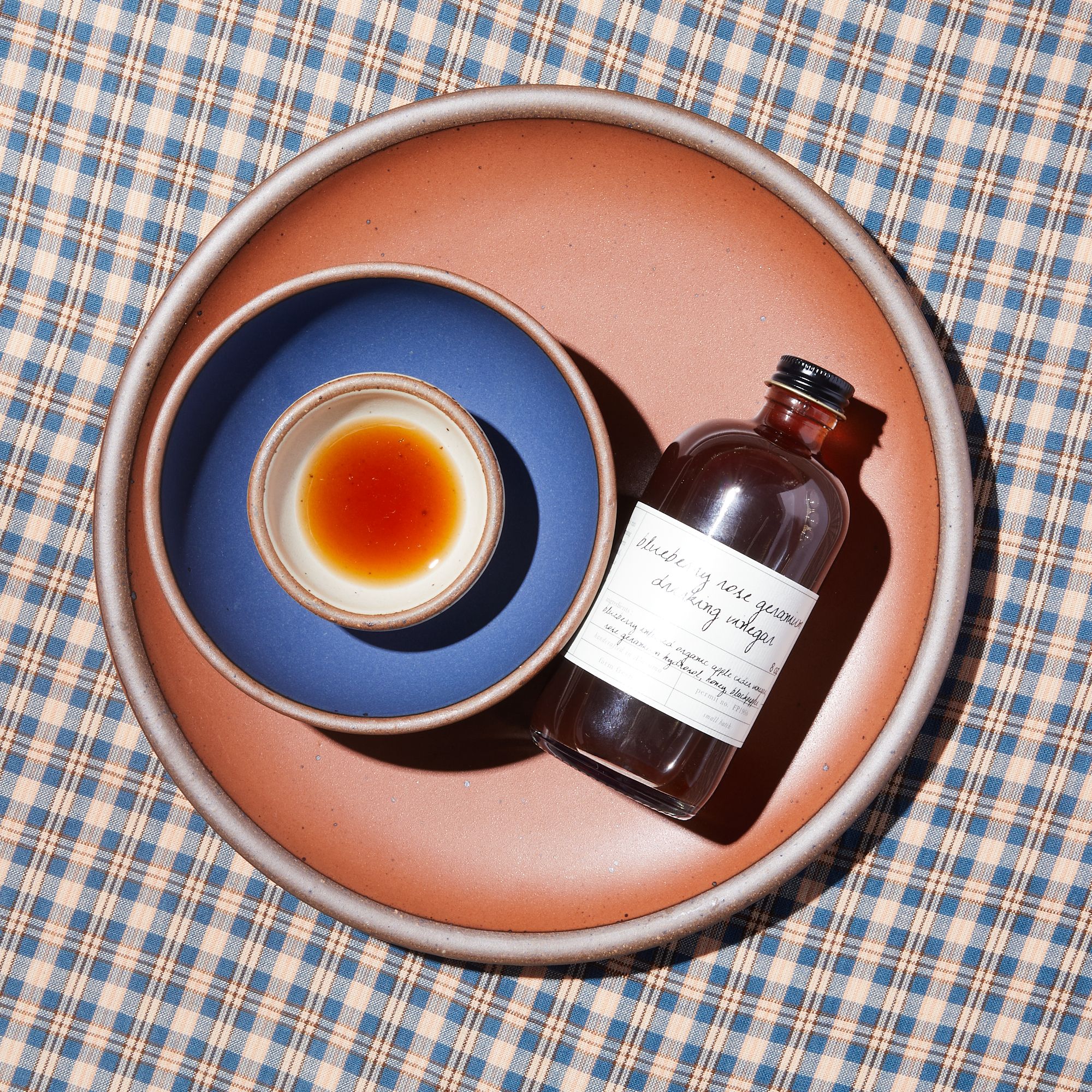 Amaro Dinner Plate with Blue Ridge Breakfast Bowl and Panna Cotta Bitty Bowl on top. Bitty Bowl is filled with drinking vinegar and a bottle of the vinegar is next to the bowls on the plate. 