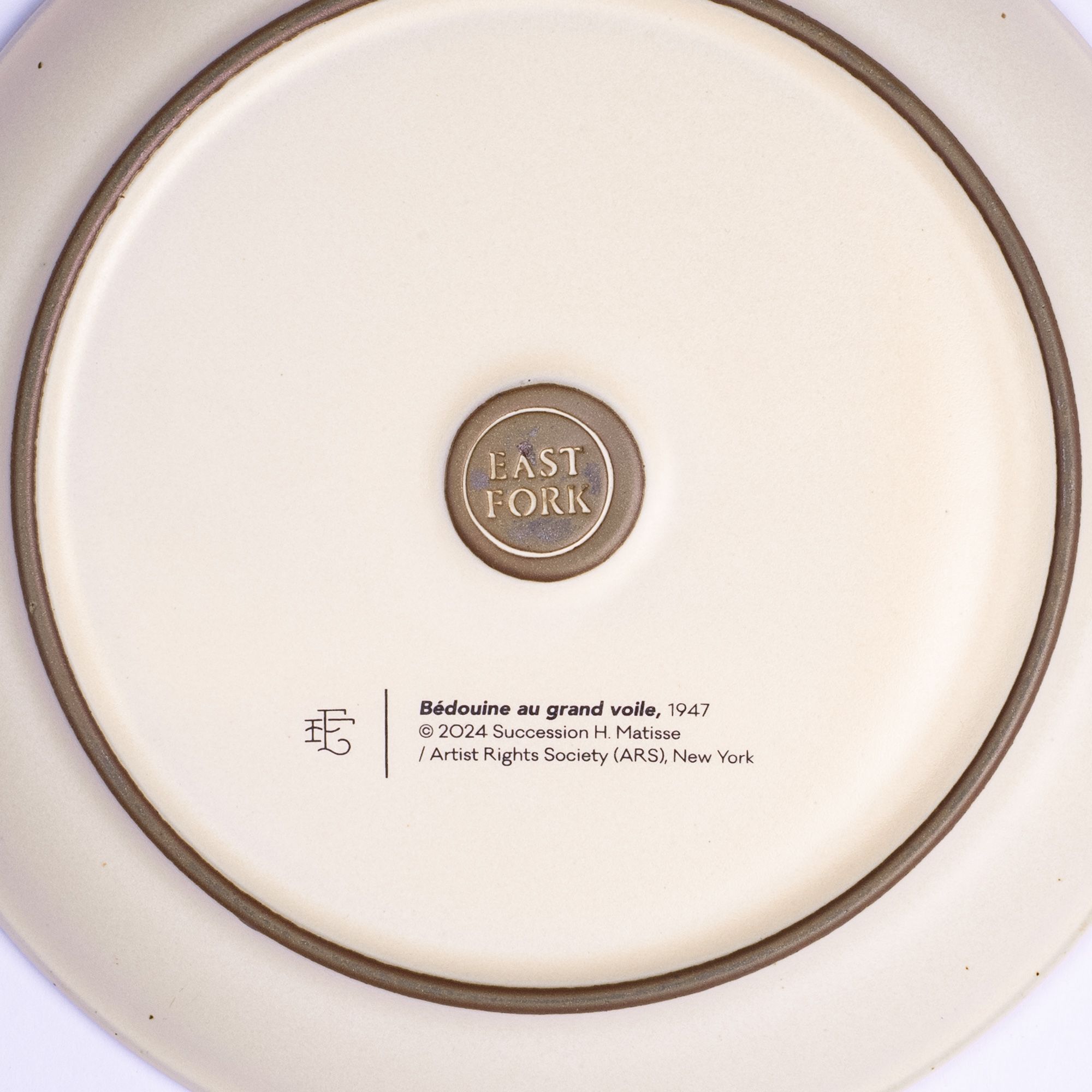The back of a side plate with an East Fork stamp with a small decal of information about the artwork, Bédouine au grand voile, by Henri Matisse.