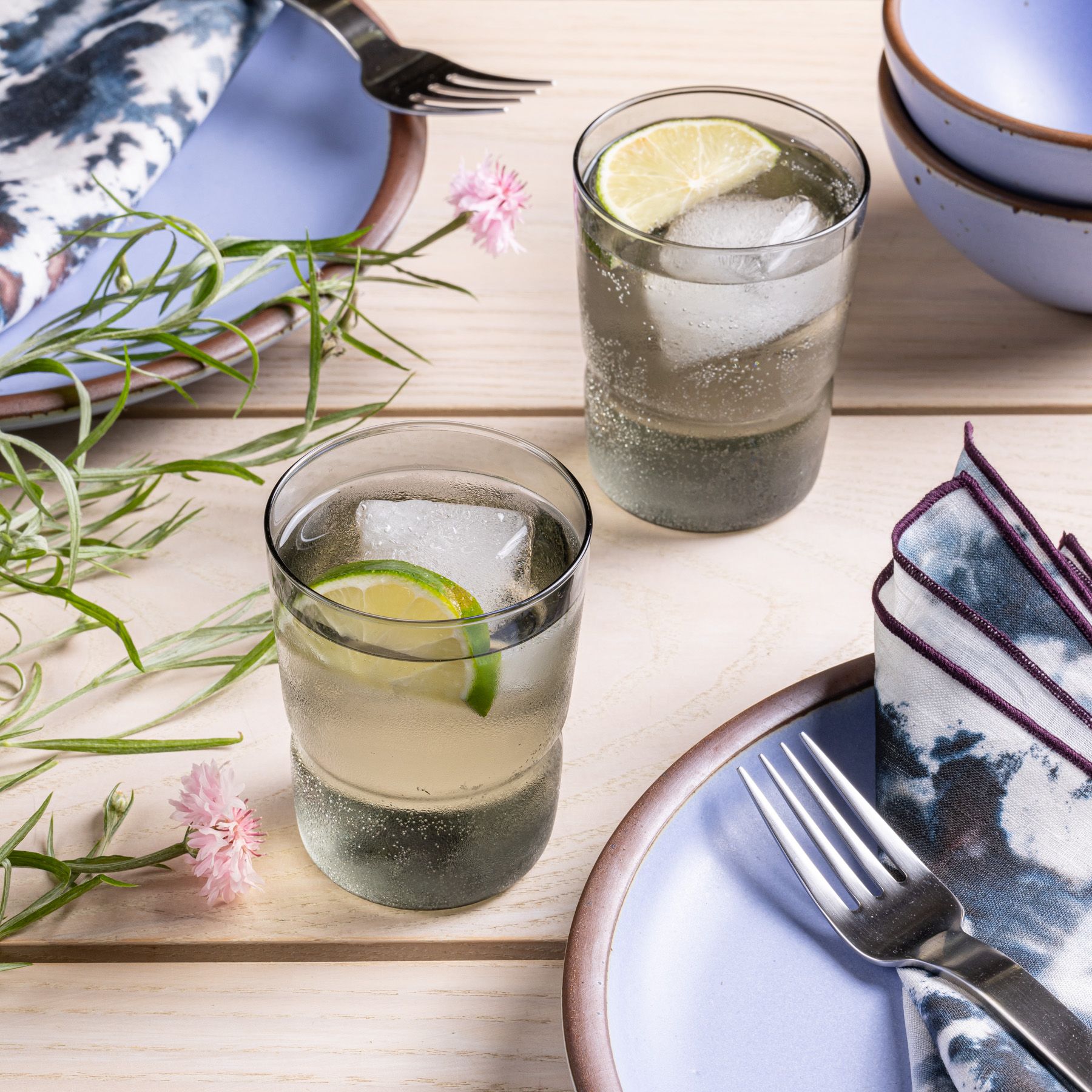 Two tumbler glasses that widens at the top in a grey color, sitting on a table with plates, and silverware