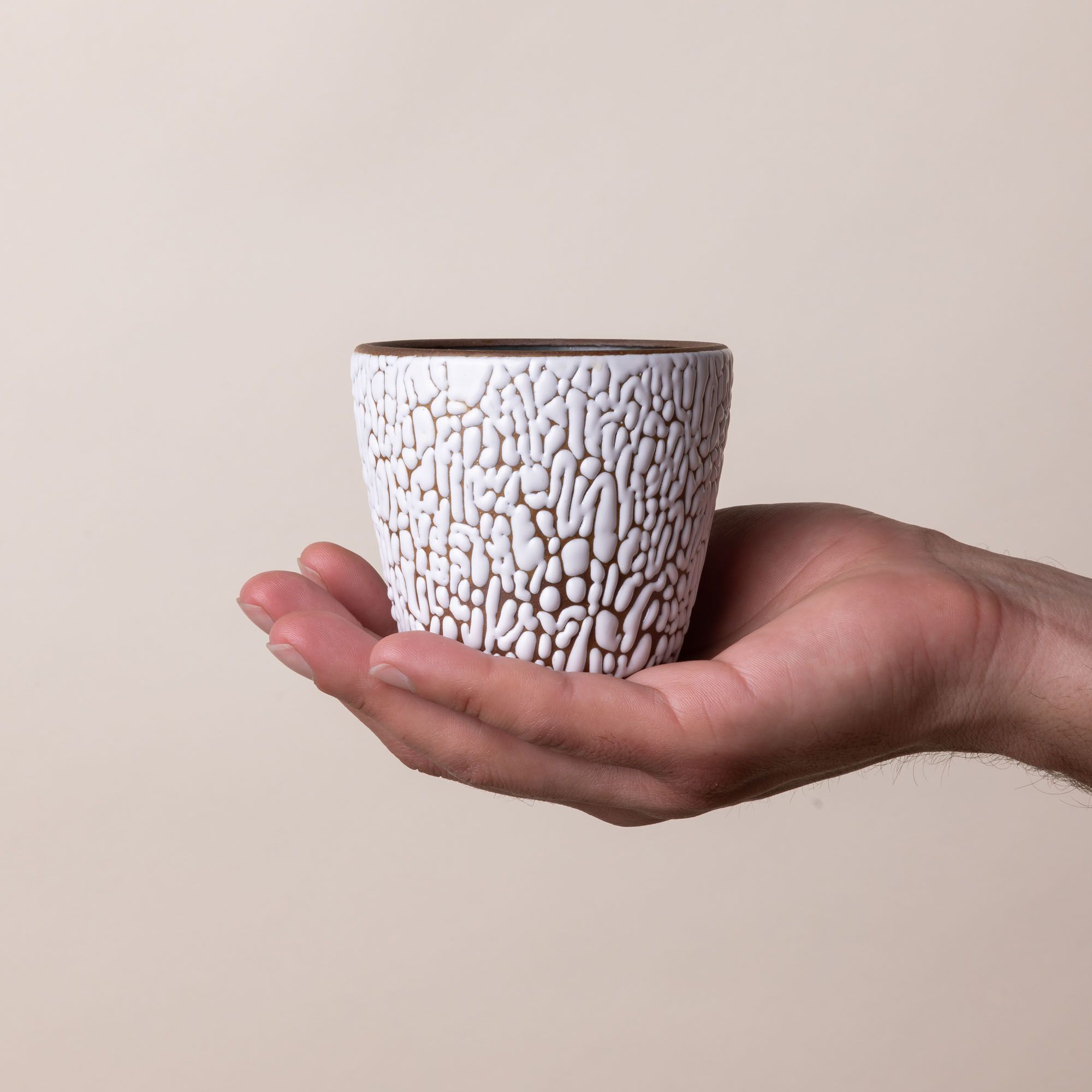 A hand holds a small ceramic cup with cracked texture and the interior being dark teal.