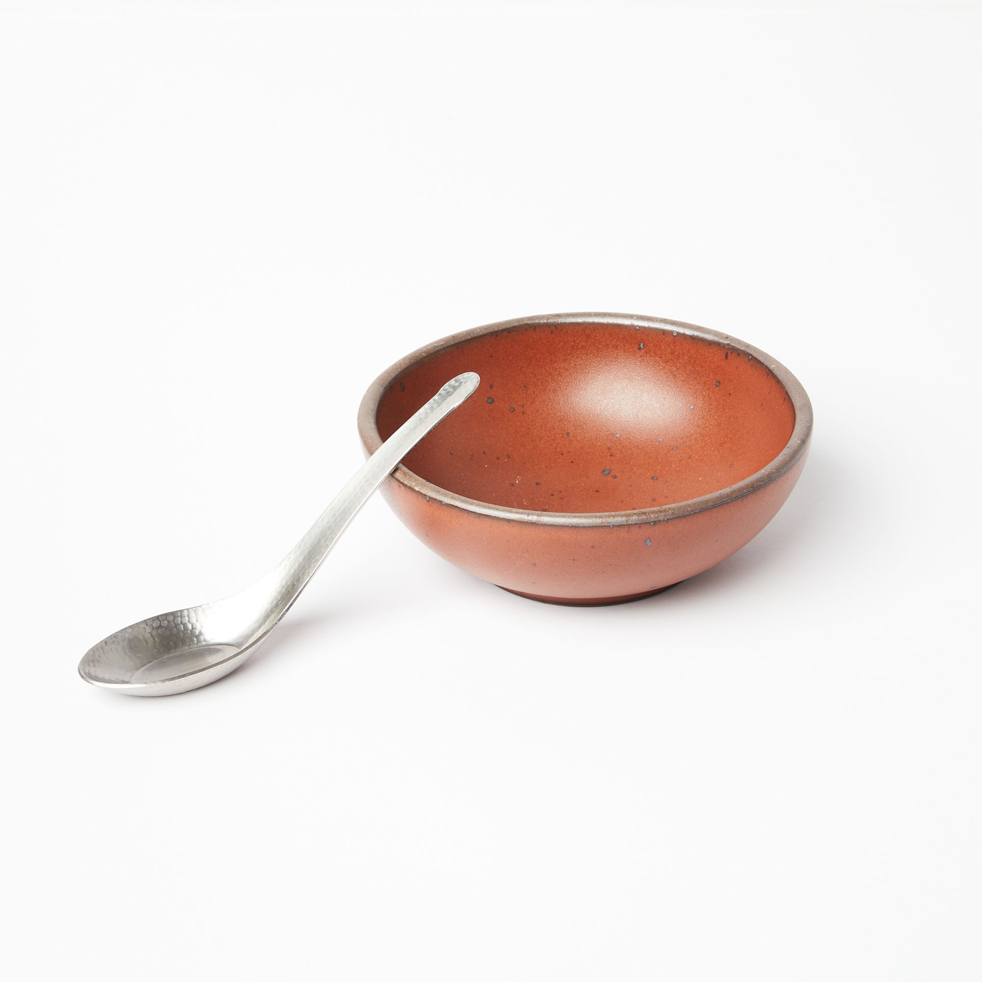 A steel Asian soup spoon with hammered finish leans on a ceramic terracotta bowl