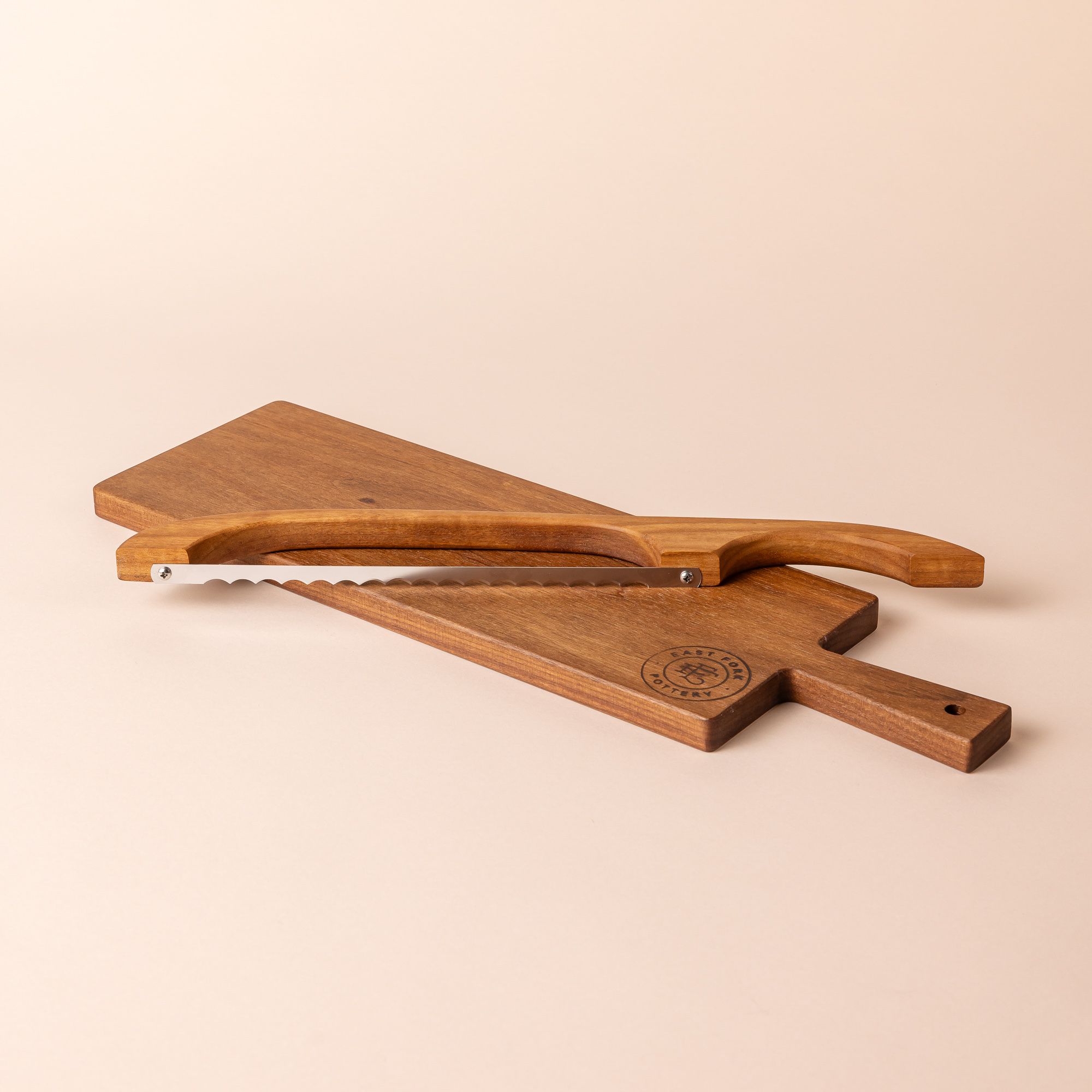 A wood rectangle bread board with an "East Fork Pottery" stamp on the corner and a handle. A matching wood bread bow sits on top of it.
