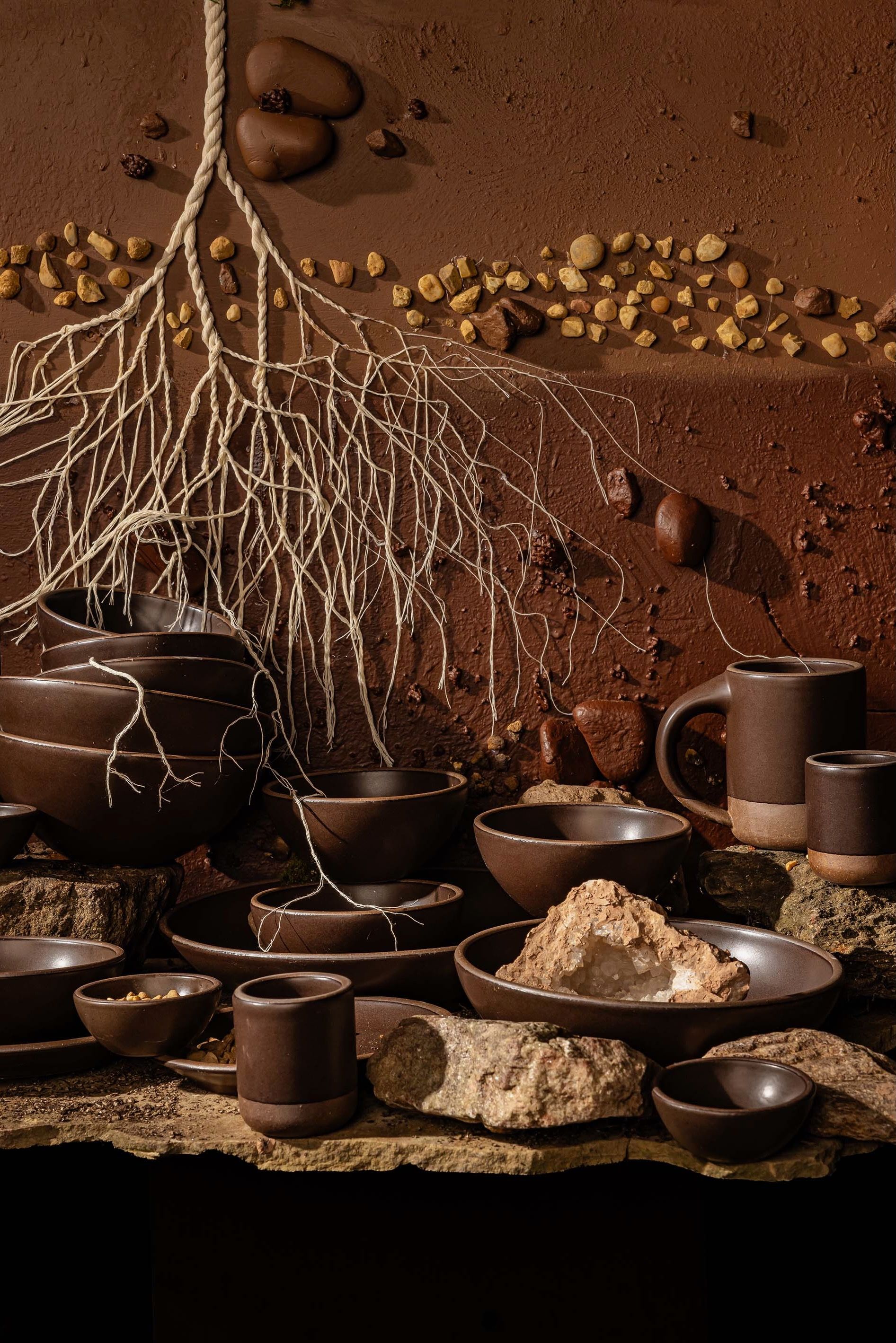 Earthy ground environment with tree roots, rocks, and dirt with various plates and bowls in a dark brown. 