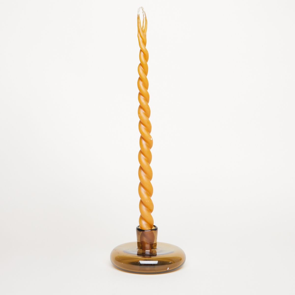 A brown glass candle holder holds a tall yellow candle that is made of two lengths of wax, twisted together.