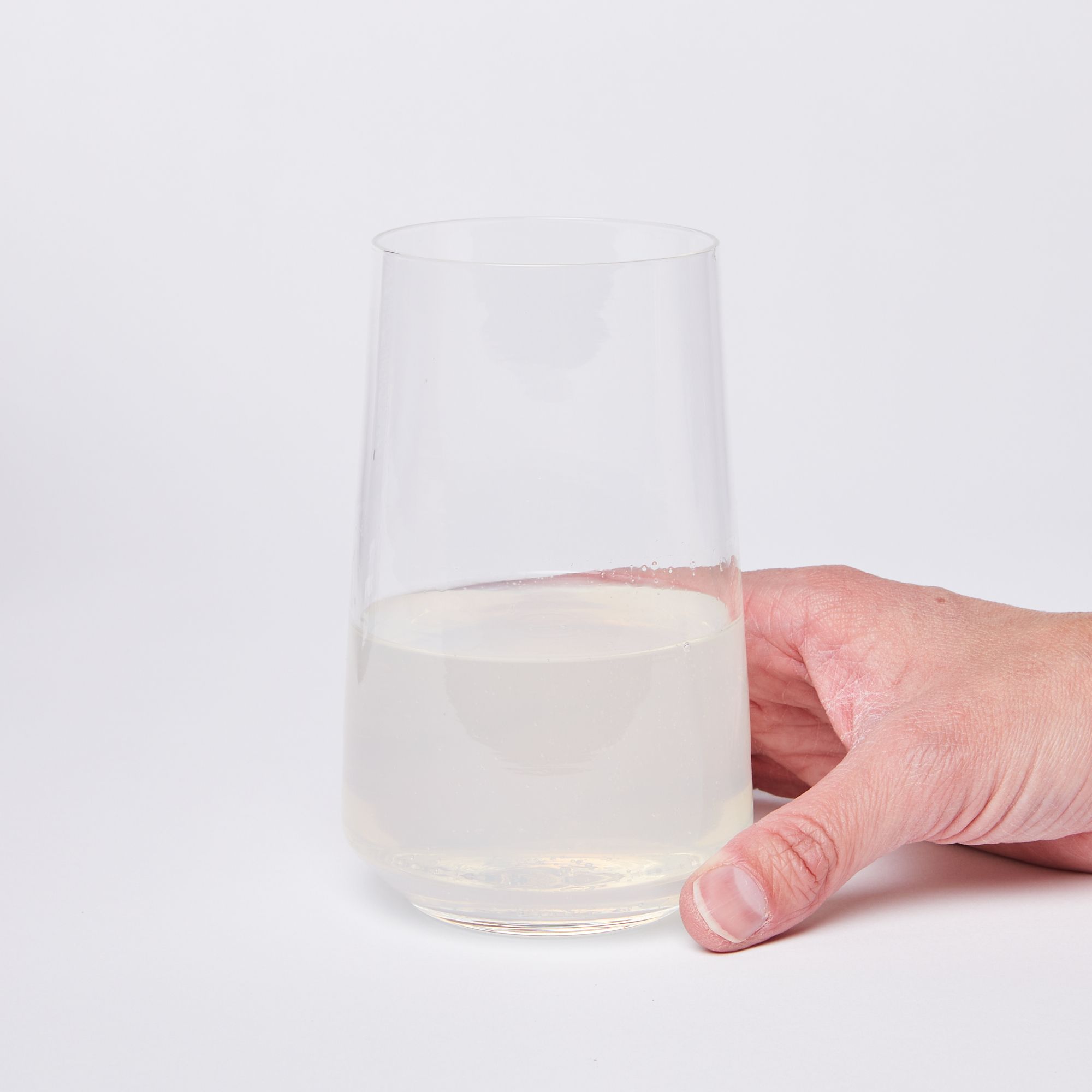 Hand holding a clear round glass half full of a semi-opaque beverage