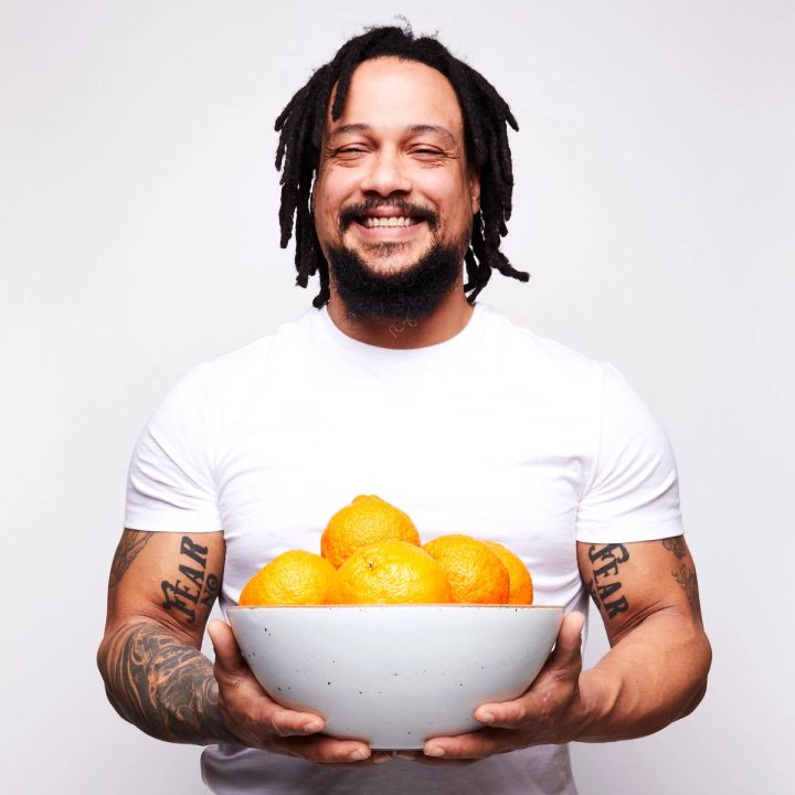 A person smiling wearing a white tee and holding a Mixing Bowl filled with oranges.