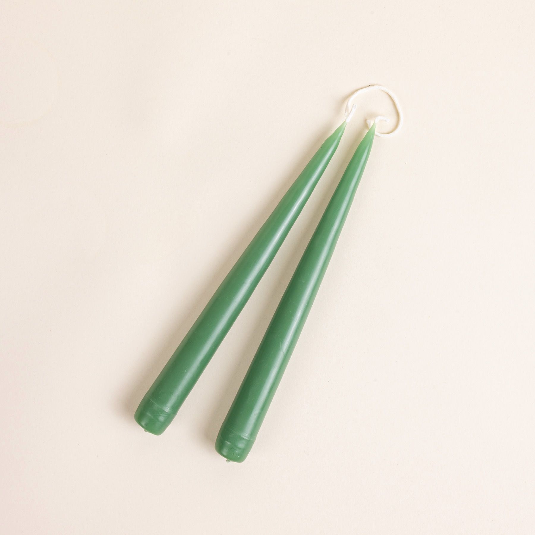 A pairs of green taper candles with the wick connected at the top.
