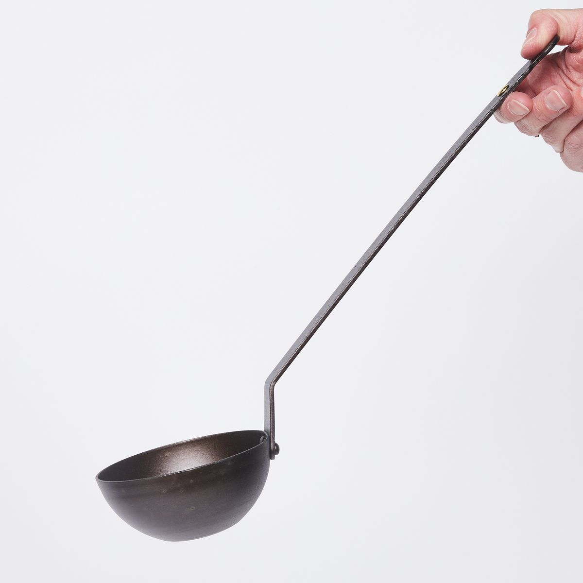 Hand holding a black metal ladle at the top of the handle in the upper right in the frame