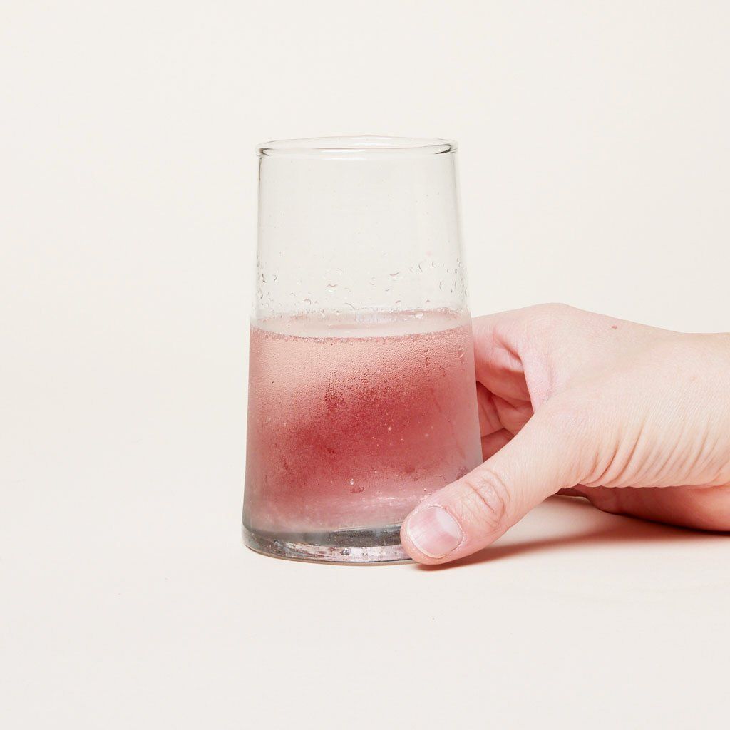 Handing holding a recycled Moroccan glassware tall glass that contains pink liquid