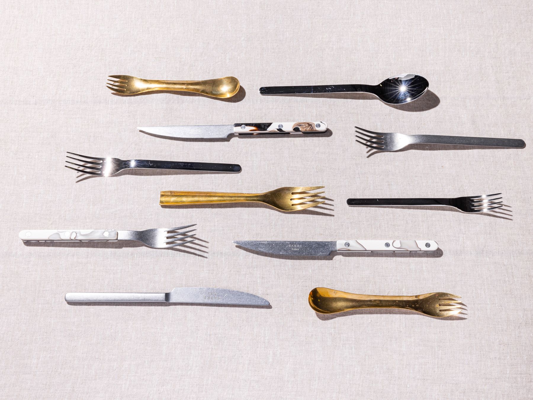 Different styles of forks, spoons, and knifes artfully lined up in parallel rows.