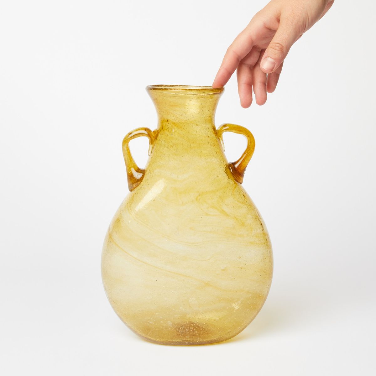 a hand touching a translucent yellow vase, narrowing at the top with two small handles
