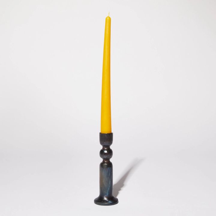 Yellow tapered beeswax candle in thin iron candle holder