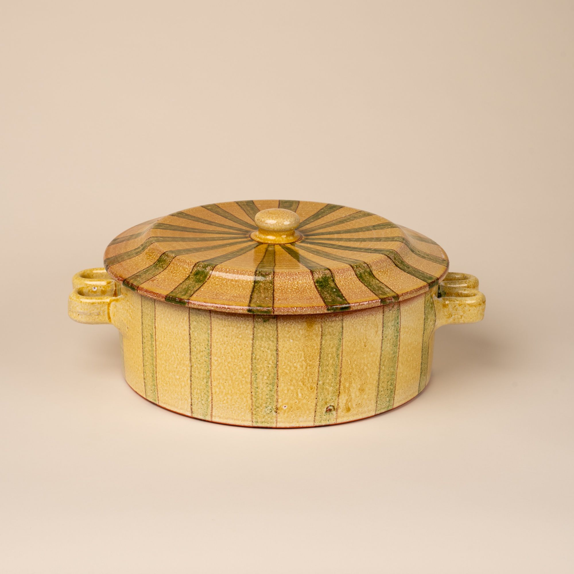 A large terracotta casserole dish with handles on each side and large lid with knob handle. The pot is striped with green and butter colors.
