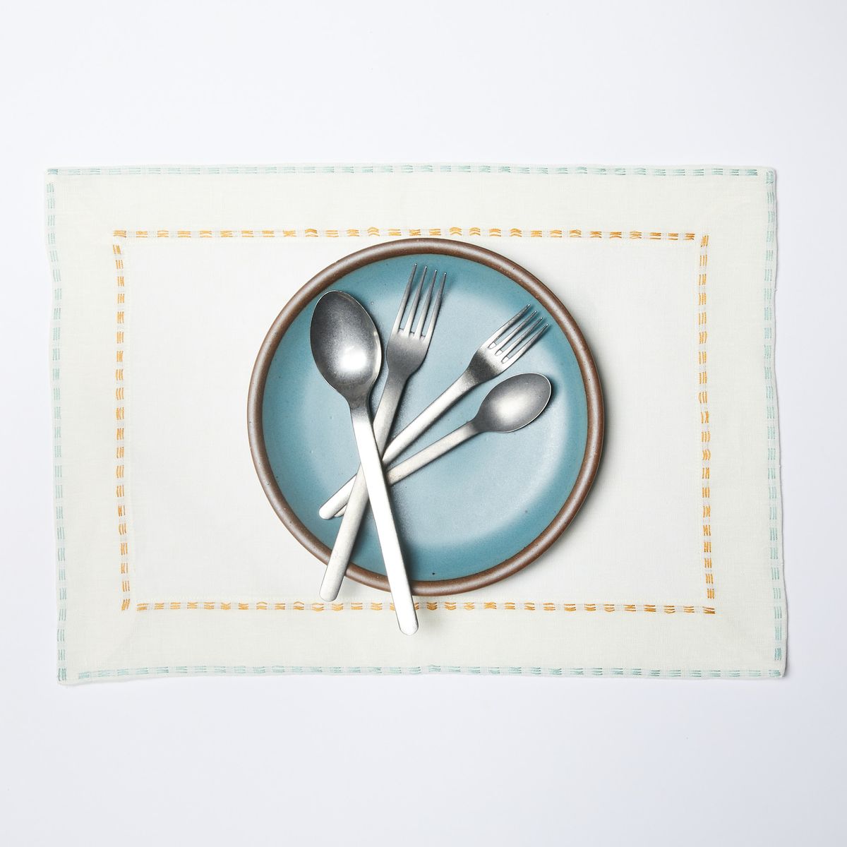 White placemat with aqua border and blue plate and silverware on top
