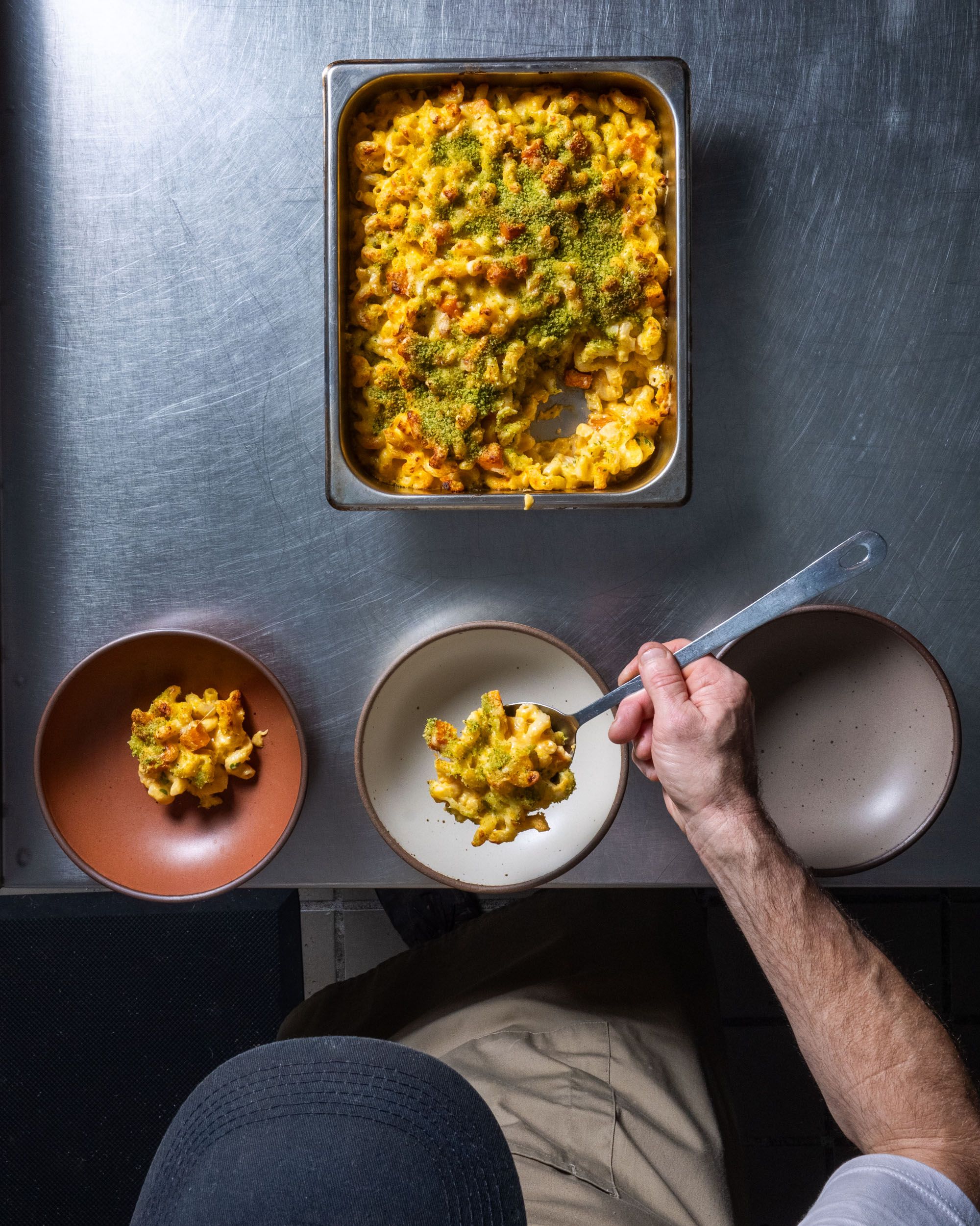 A chef holds a spoon and is scooping some gourmet mac and cheese into bowls from a casserole dish.