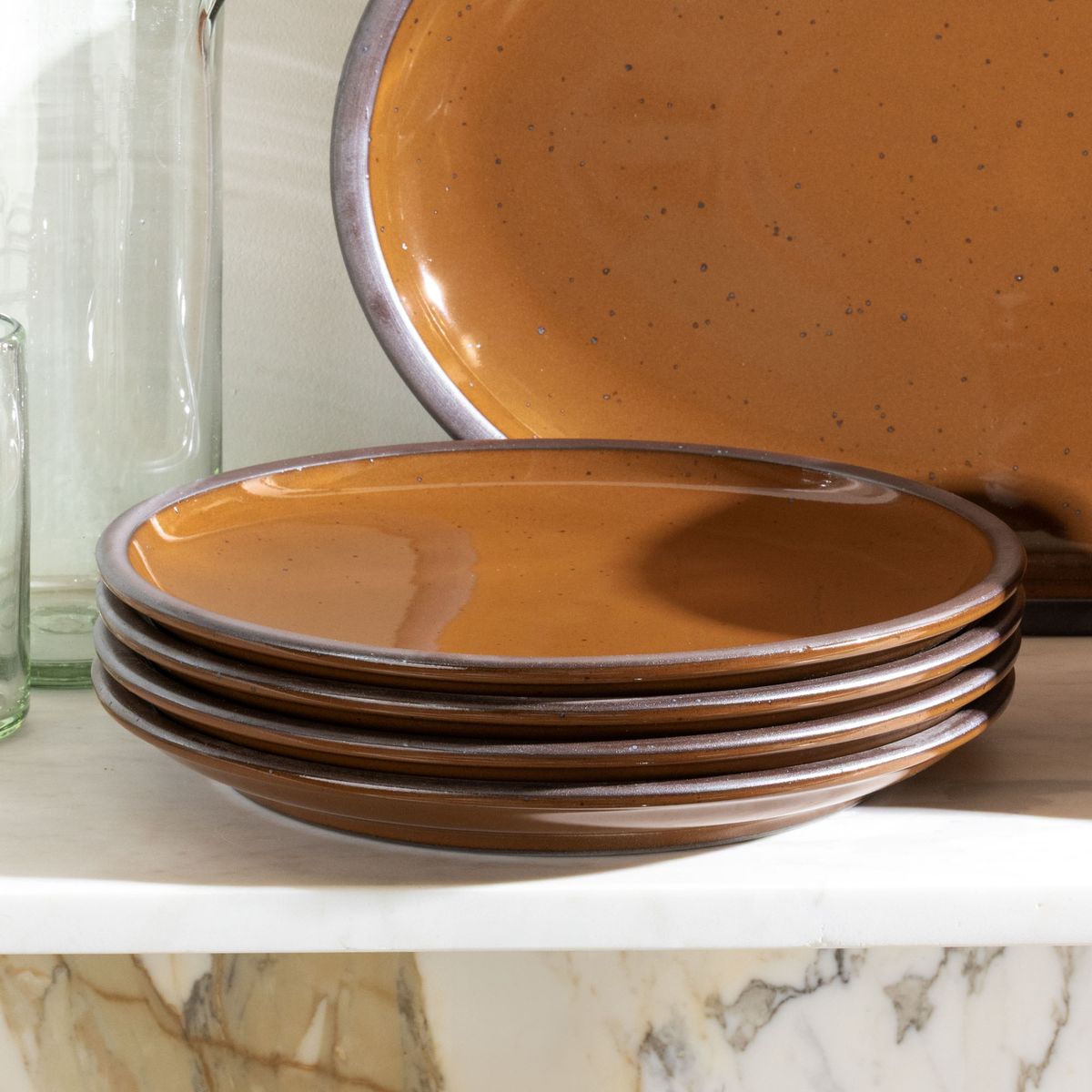A stack of 4 dinner sized ceramic plates in glossy caramel brown on a white shelf