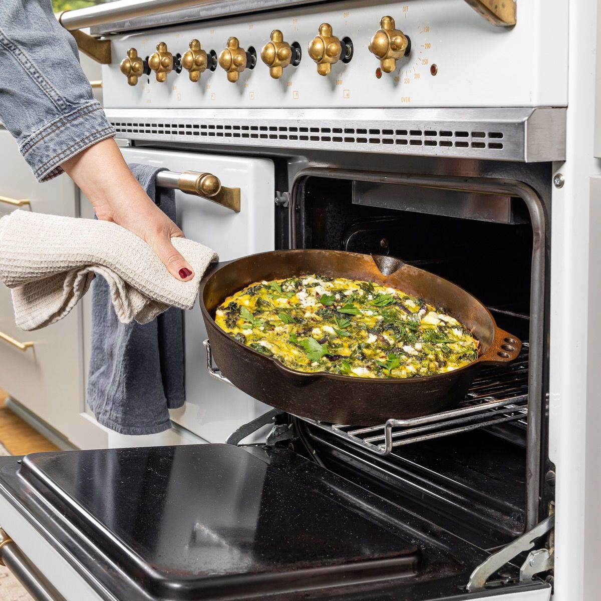 Hands hold a kitchen towel to carry a cast iron skillet out of the oven