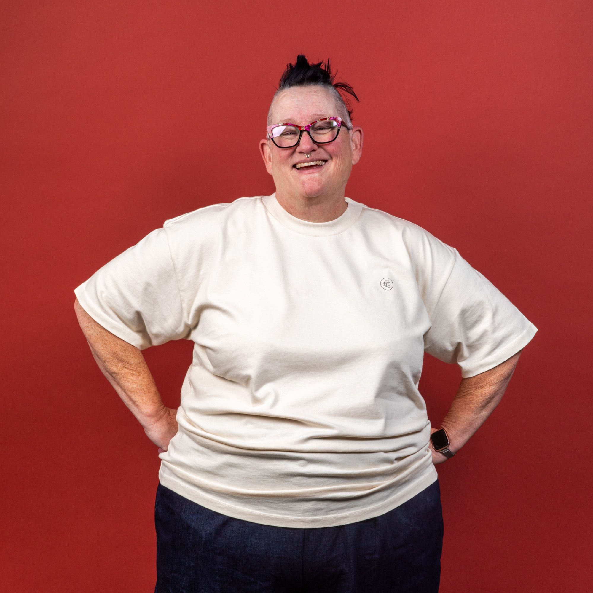 Model wearing the t-shirt and smiling at the camera with hands on hips and wearing pink glasses