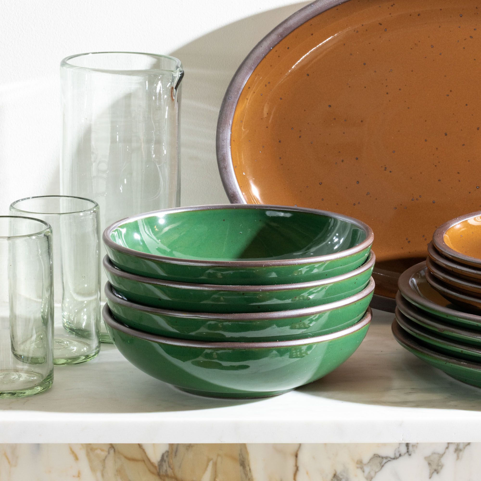A stack of 4 dinner-sized shallow ceramic bowls in a glossy emerald green color on a white