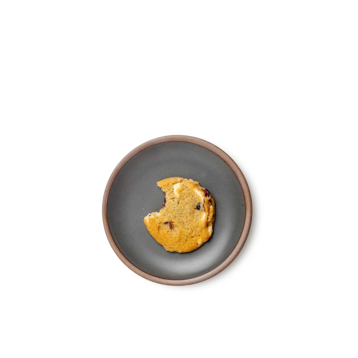 A half-eaten cookie on a dessert sized ceramic plate in a cool, medium grey color featuring iron speckles and an unglazed rim