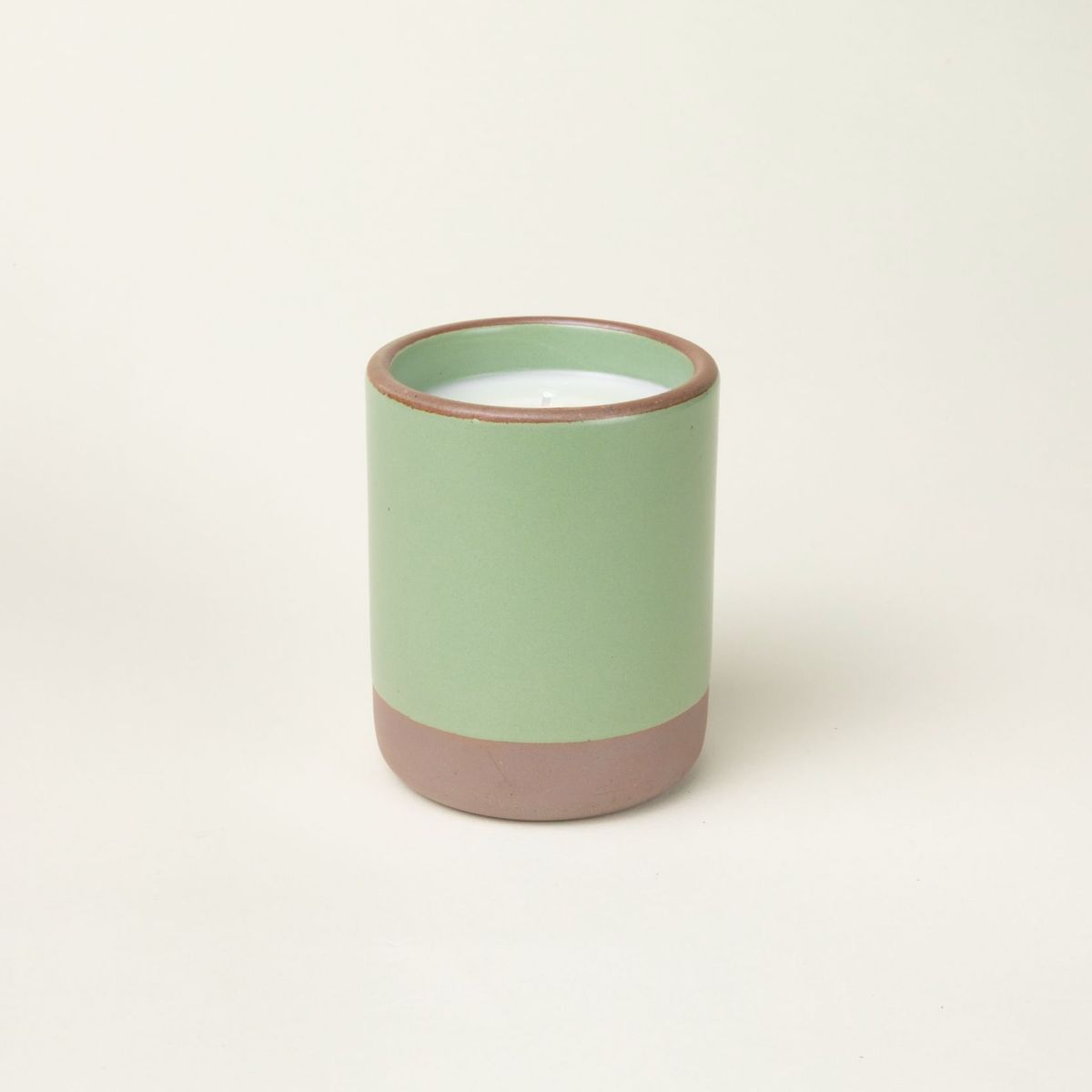 A candle in a large ceramic vessel dipped in a sage green color.