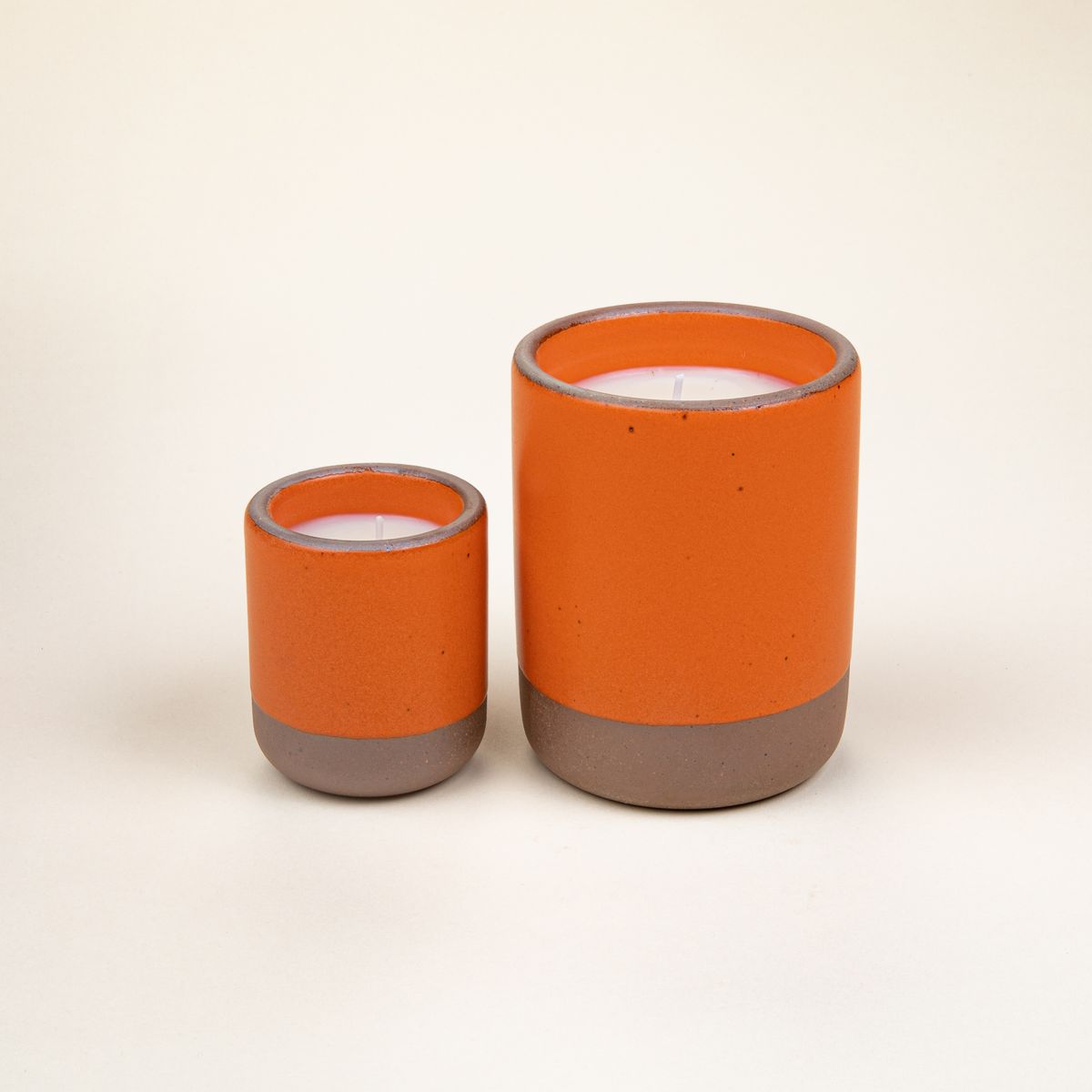 Small and large ceramic vessels in a bold orange color with poured candles inside each.